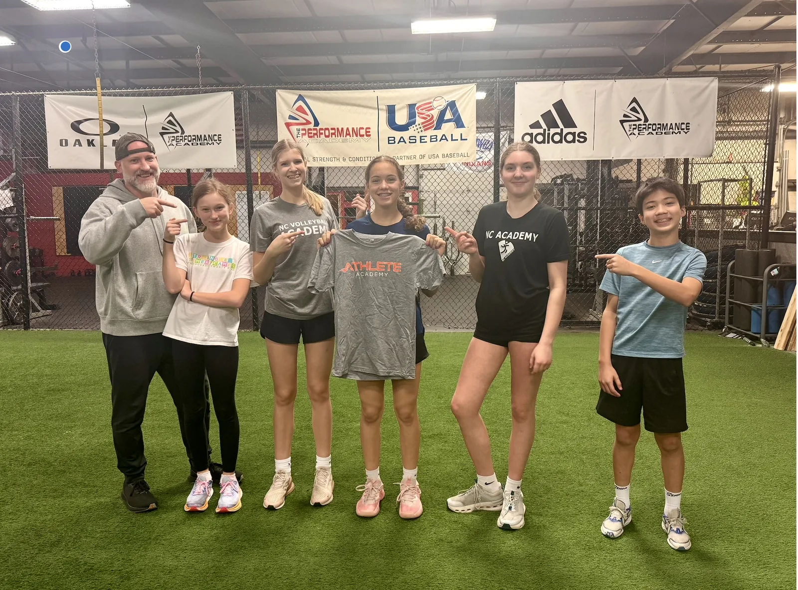 Coach Aaron and a group of athletes pointing at the Athlete Academy shirt Lilly earned at her advancement