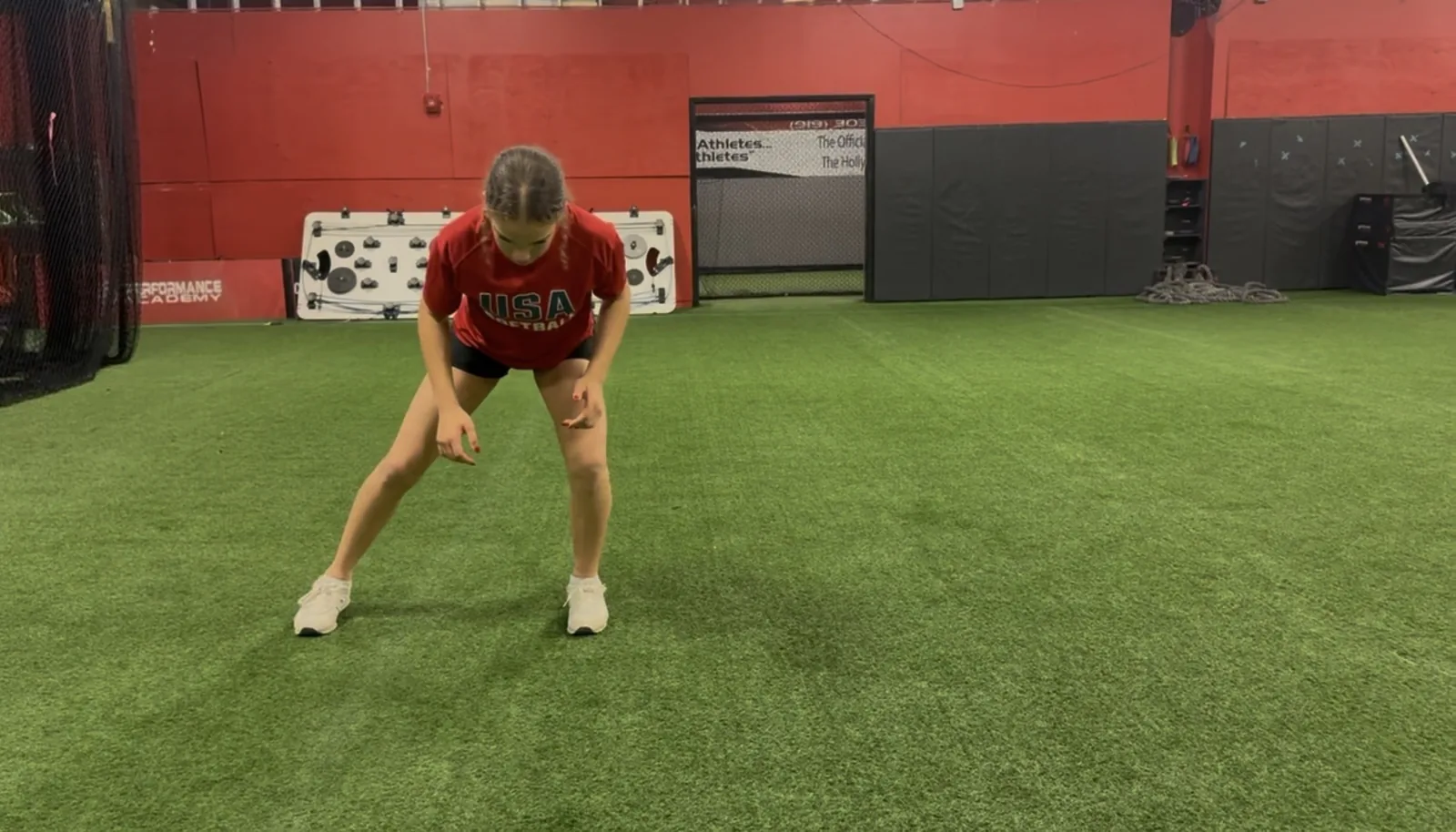 A softball athlete driving sideways out of a low athletic stance on the turf