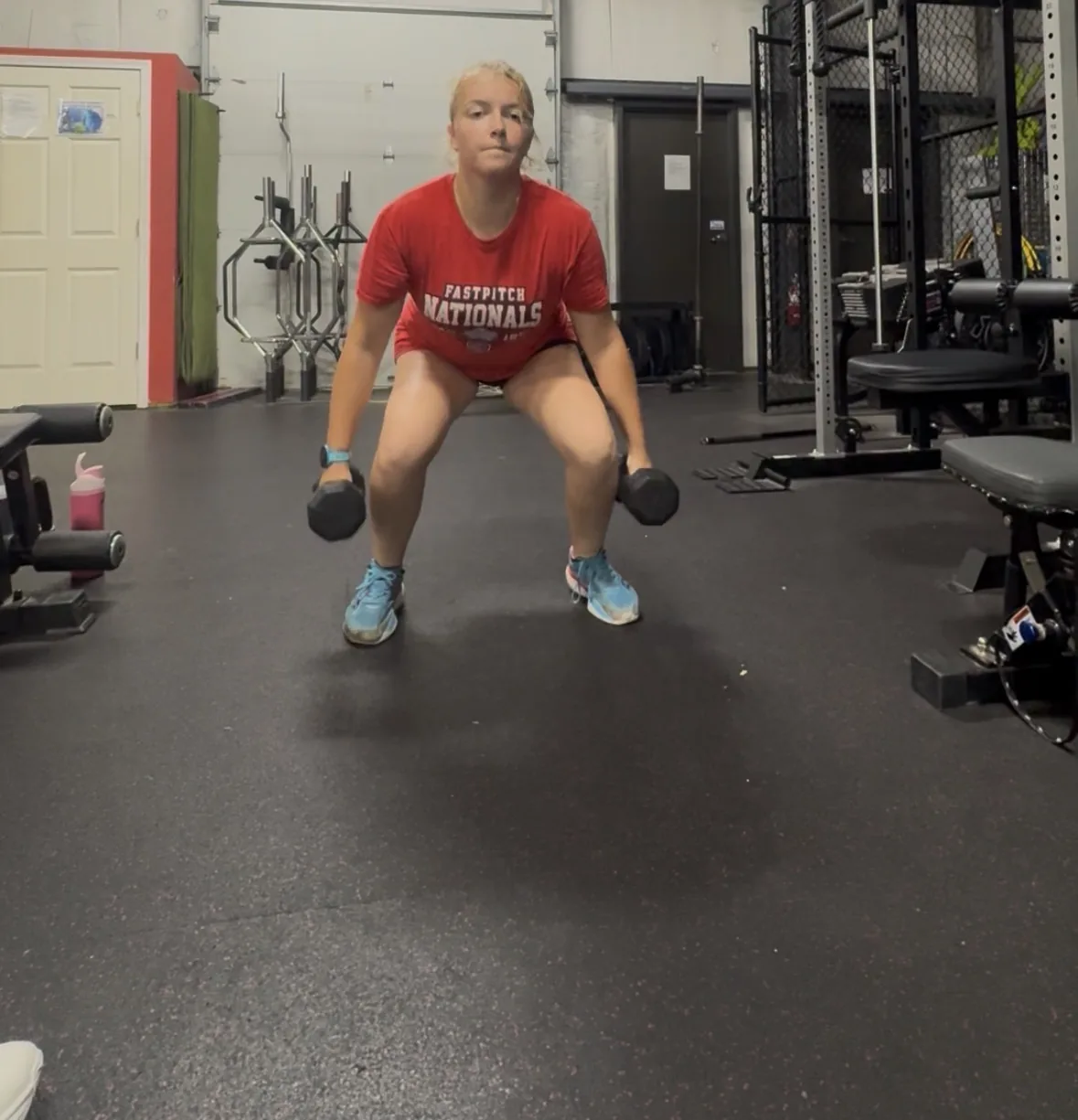 A softball athlete absorbing the bottom of a squat with dumbbells at her sides, feet flat and knees tracking forward